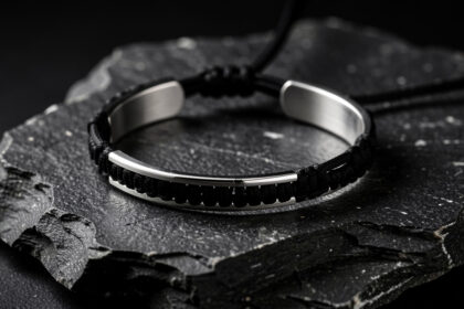 Bracelet menottes en argent poli monté sur un cordon noir et posé sur une pierre sombre, éclairé par une lumière d’atelier.